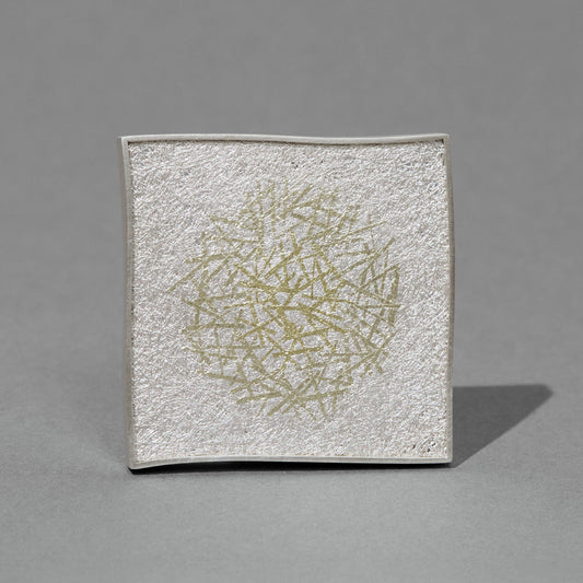 Square textured white silver brooch with gold abstract design on a gray background